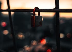 Rusty padlock on a fence with city bokeh lights and sunset backdrop.